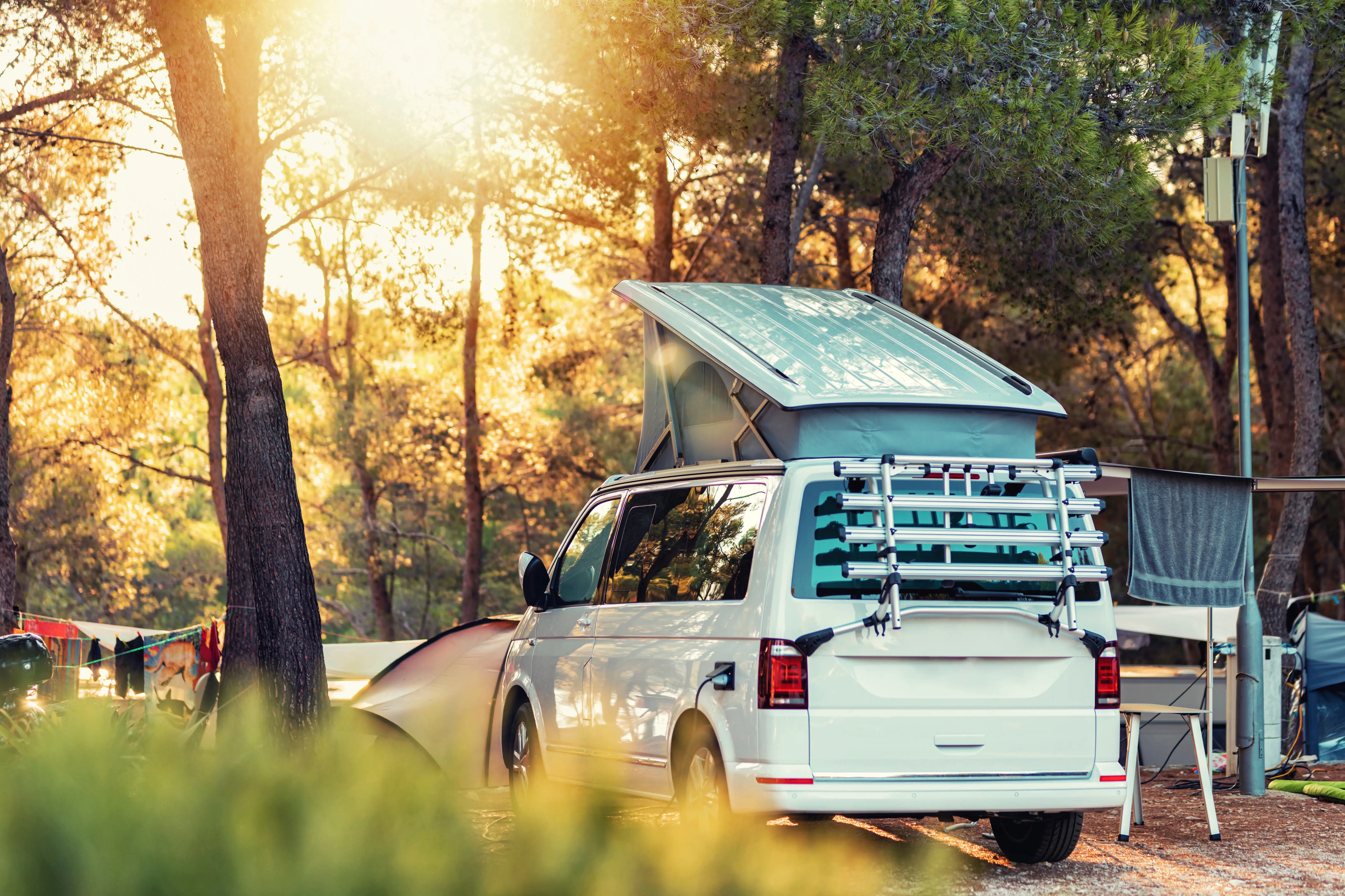 Campervan parked up at a campsite, with its top up and electric connected. Sun shining through the trees