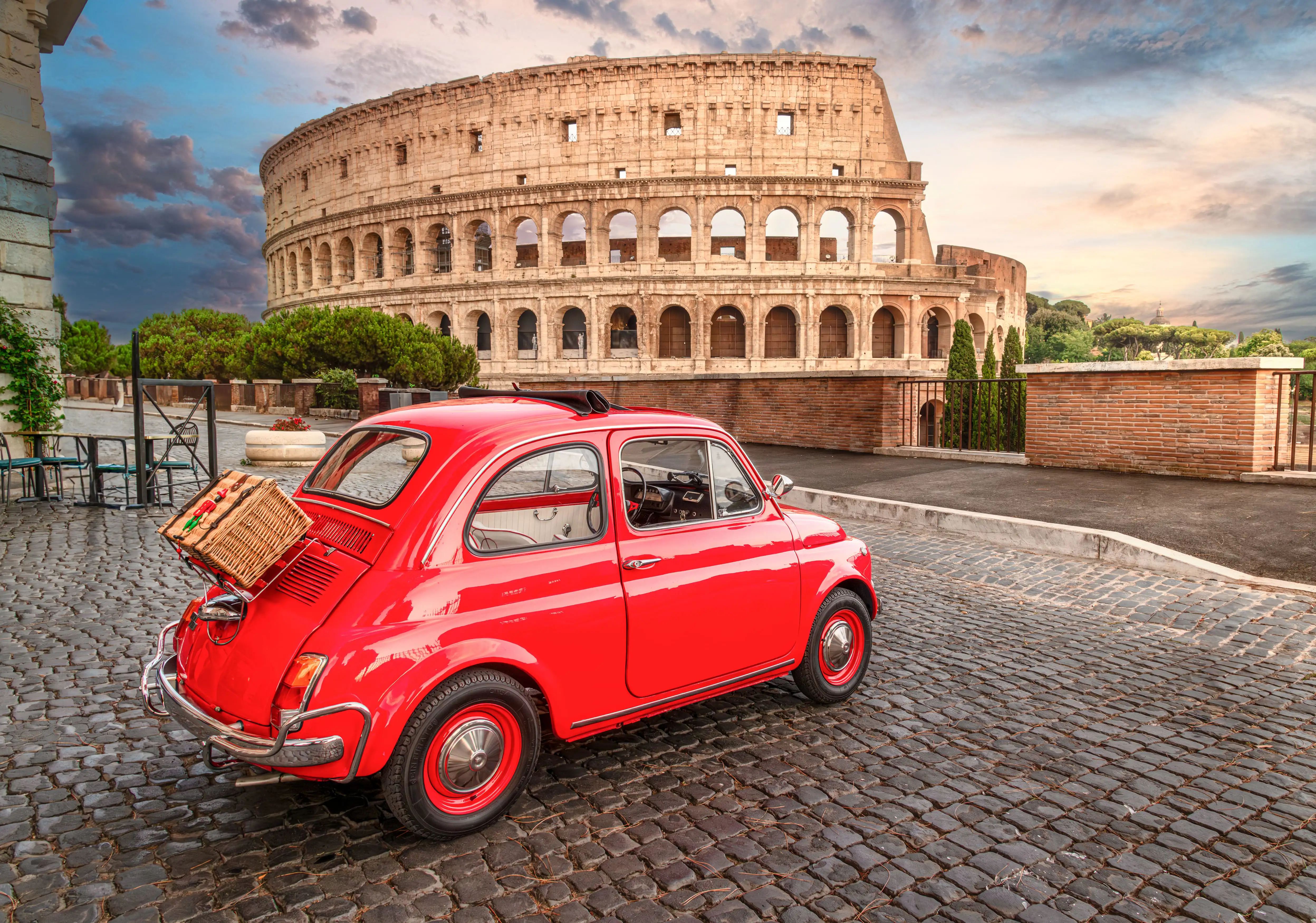 A small red retro car parked on cobbled streets near the Colosseum in Rome