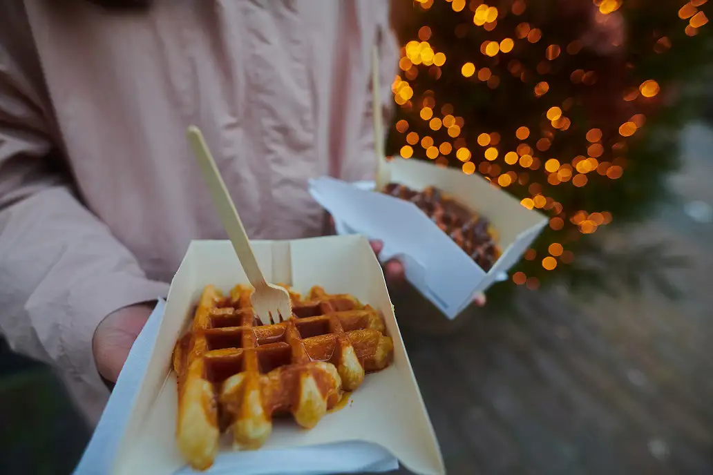 A person presents a tray of waffles in front of a beautifully decorated Christmas tree.