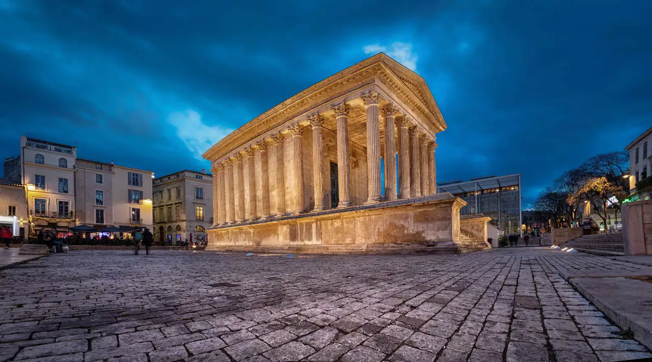 The Maison Carrée in Nîmes illuminated at night, showcasing its classical architecture with bright lights