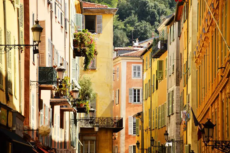 Charming narrow streets of Nice's old town, looking up at colourful buildings adorned with plants on terraces.