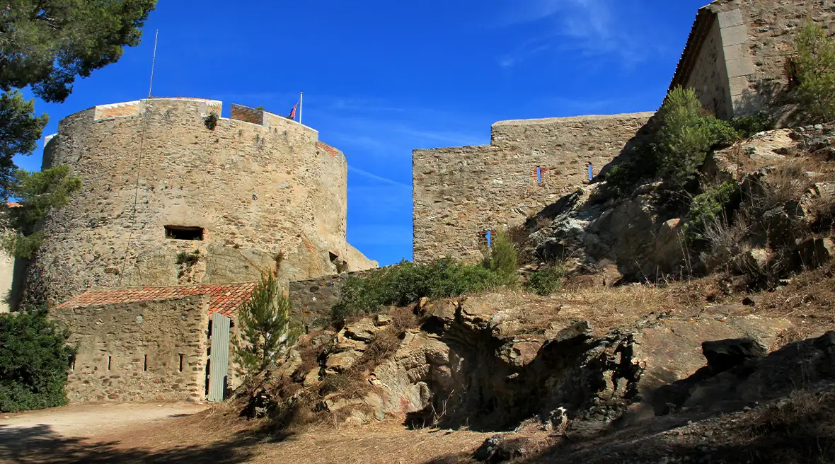 large stone building with wide tower and rocks surrounding it under blue sky