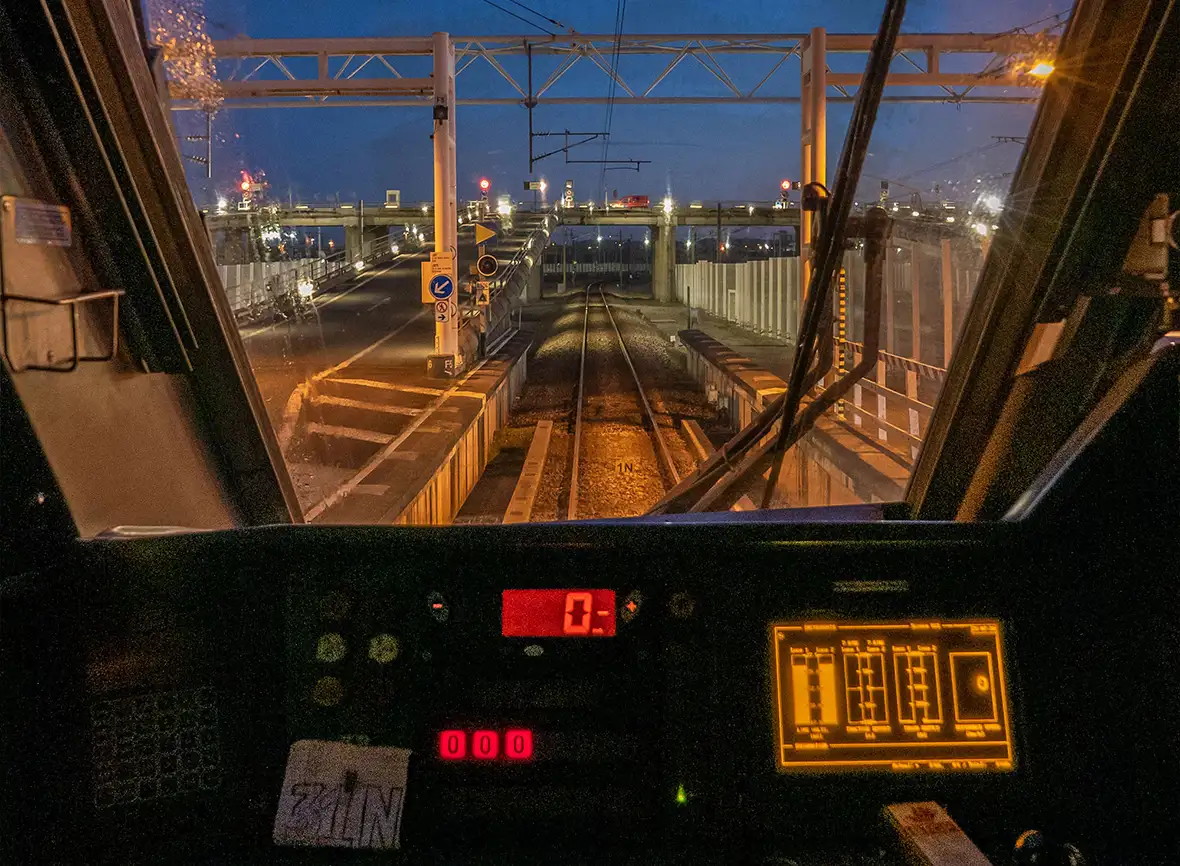 A view of the Eurotunnel track ahead of a driver from inside the cabin with controls lit up and a blue night sky with rain on the window