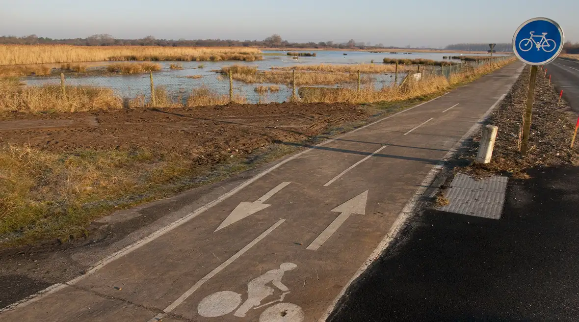 A two-way tarmac path that runs between a road on one side and a salt marsh on the other
