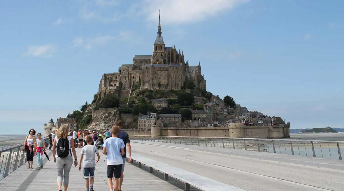 Family groups walking on a causeway towards an island on a hill, Mont Saint-Michel, with an old well preserved abbey or castle at the peak