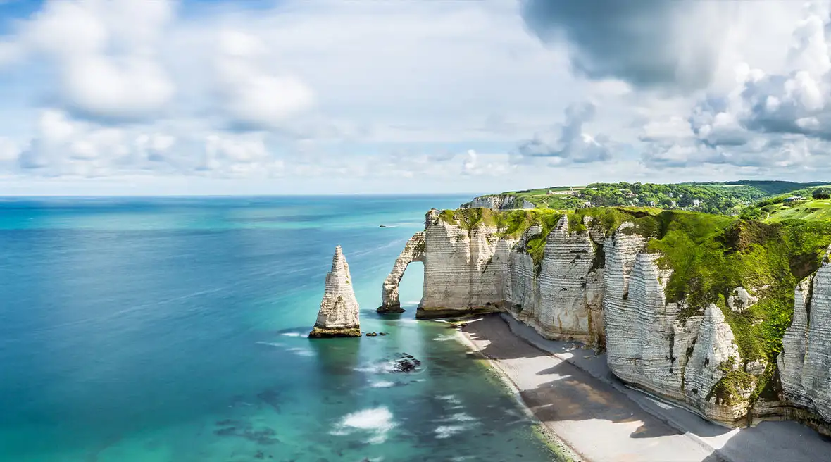 View of the white cliffs of Étretat, the pebbled beach and a blue sky with white clouds