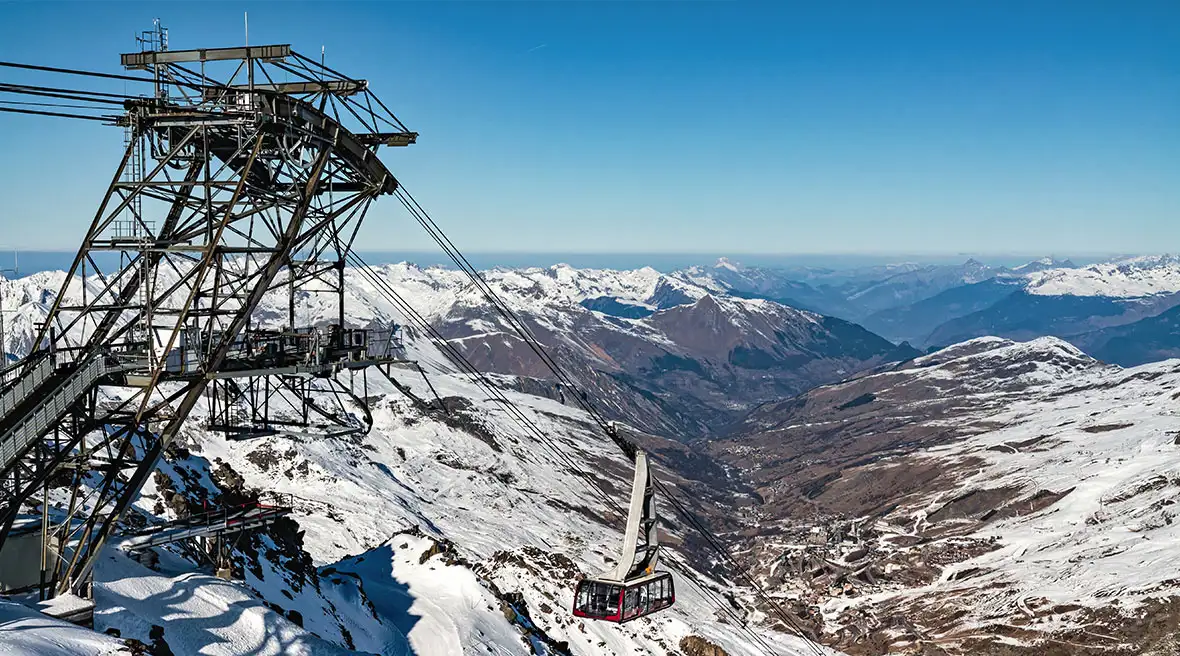 Metal enclosed ski lift at the top of a mountain with a car rising up to the top