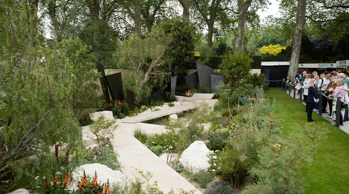 Modernistische tuin met groene struiken en witte structuren, aan de zijkant kijken mensen vanaf een afgezet pad