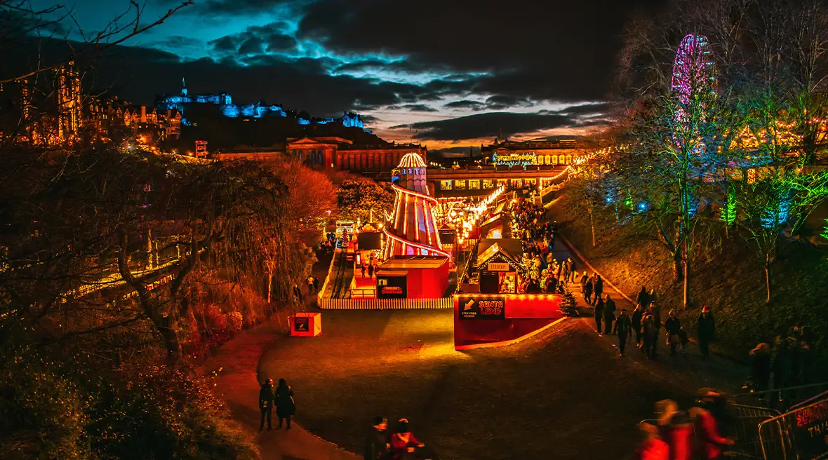 Afstandsfoto van de kerstmarkt in Edinburgh met het opgelichte reuzenrad in de achtergrond.