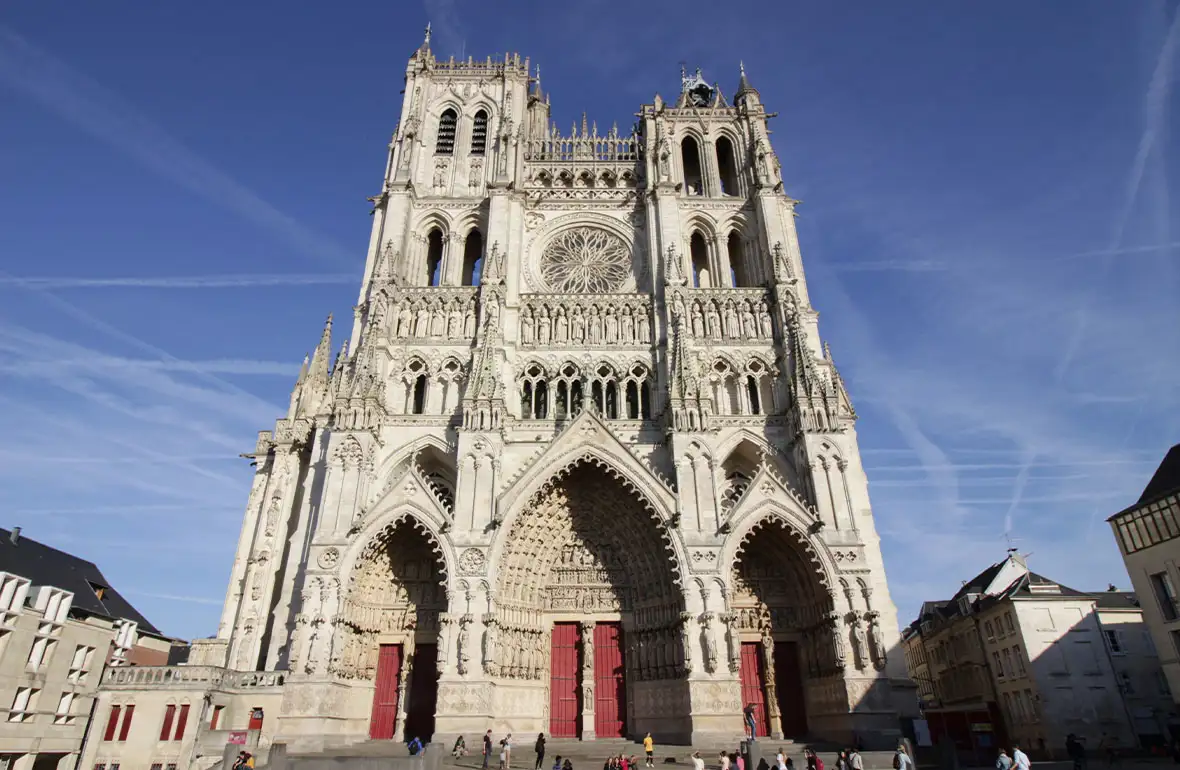 Large stone cathedral with decorative details and large red doors looming up into a blue sky