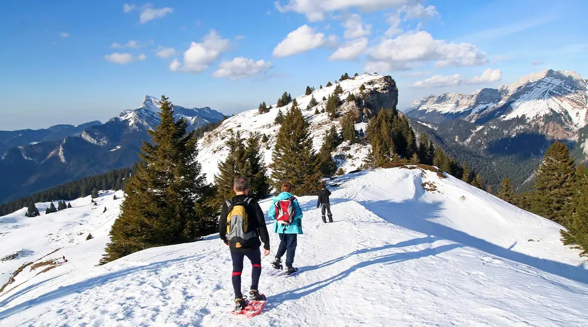 Group of friends snowshoeing over a mountain range covered in fluffy white snow