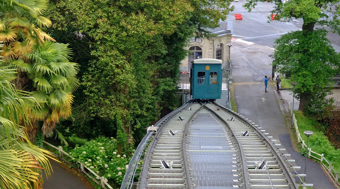 View of the green Pau Funicular railway from the top platform travelling up two tracks past green trees