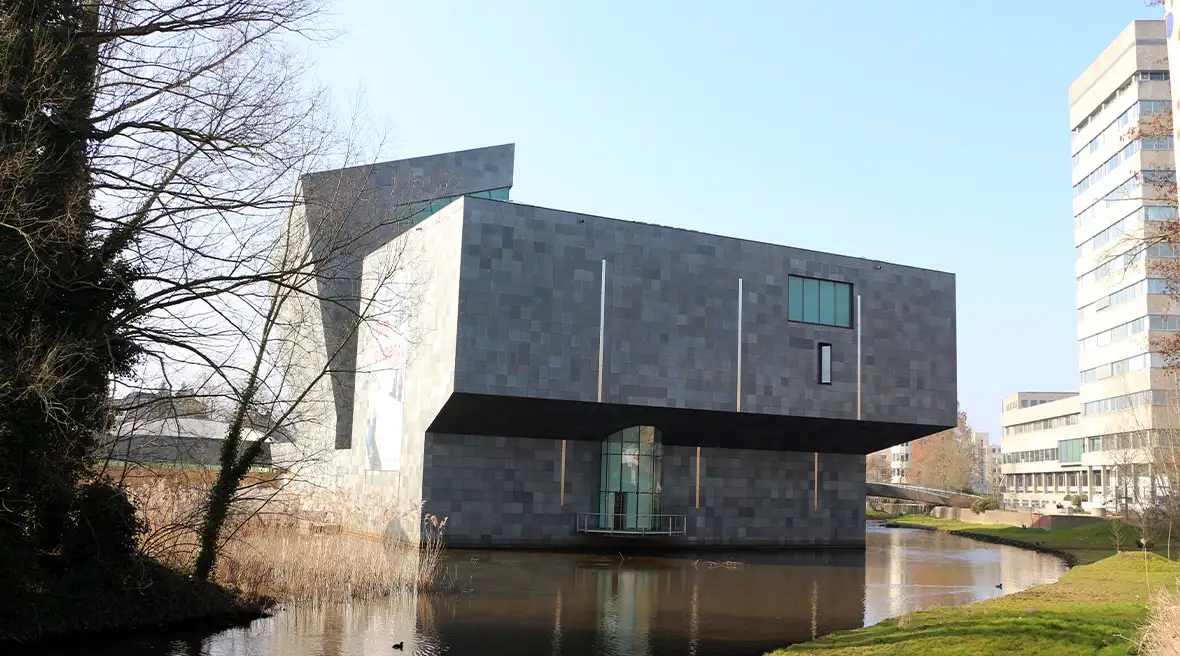 A Brutalist-style cultural building backing onto a river in an urban area