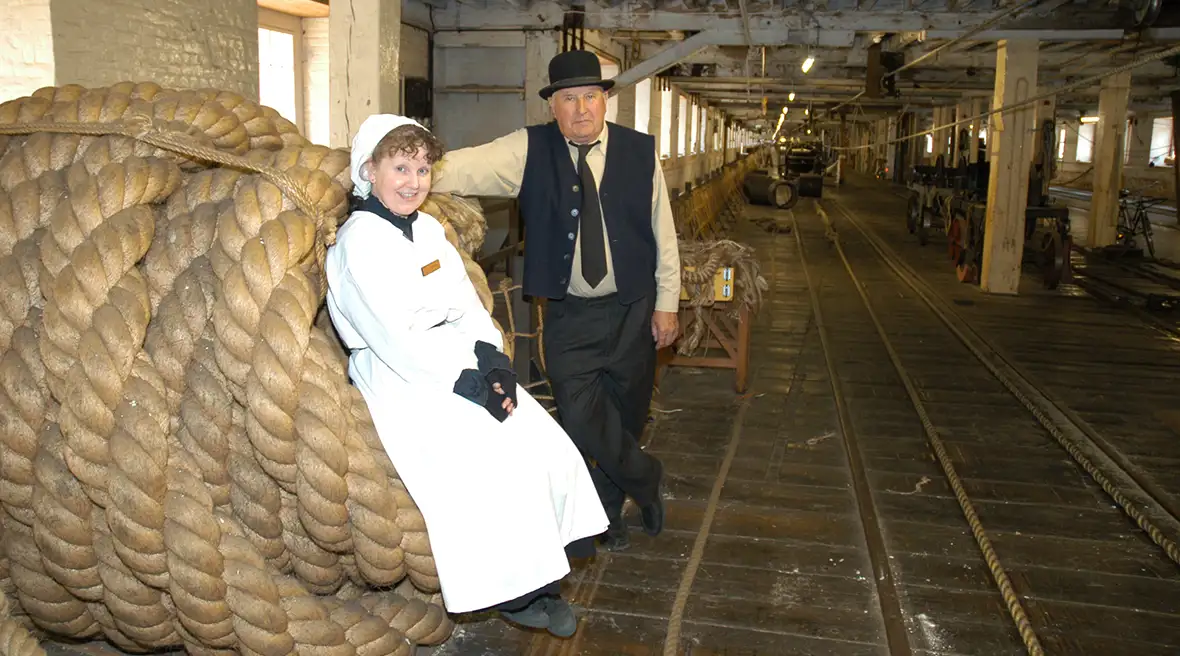 man en vrouw in Victoriaanse kleding poseren bij een bundel touw in de touwslagerij