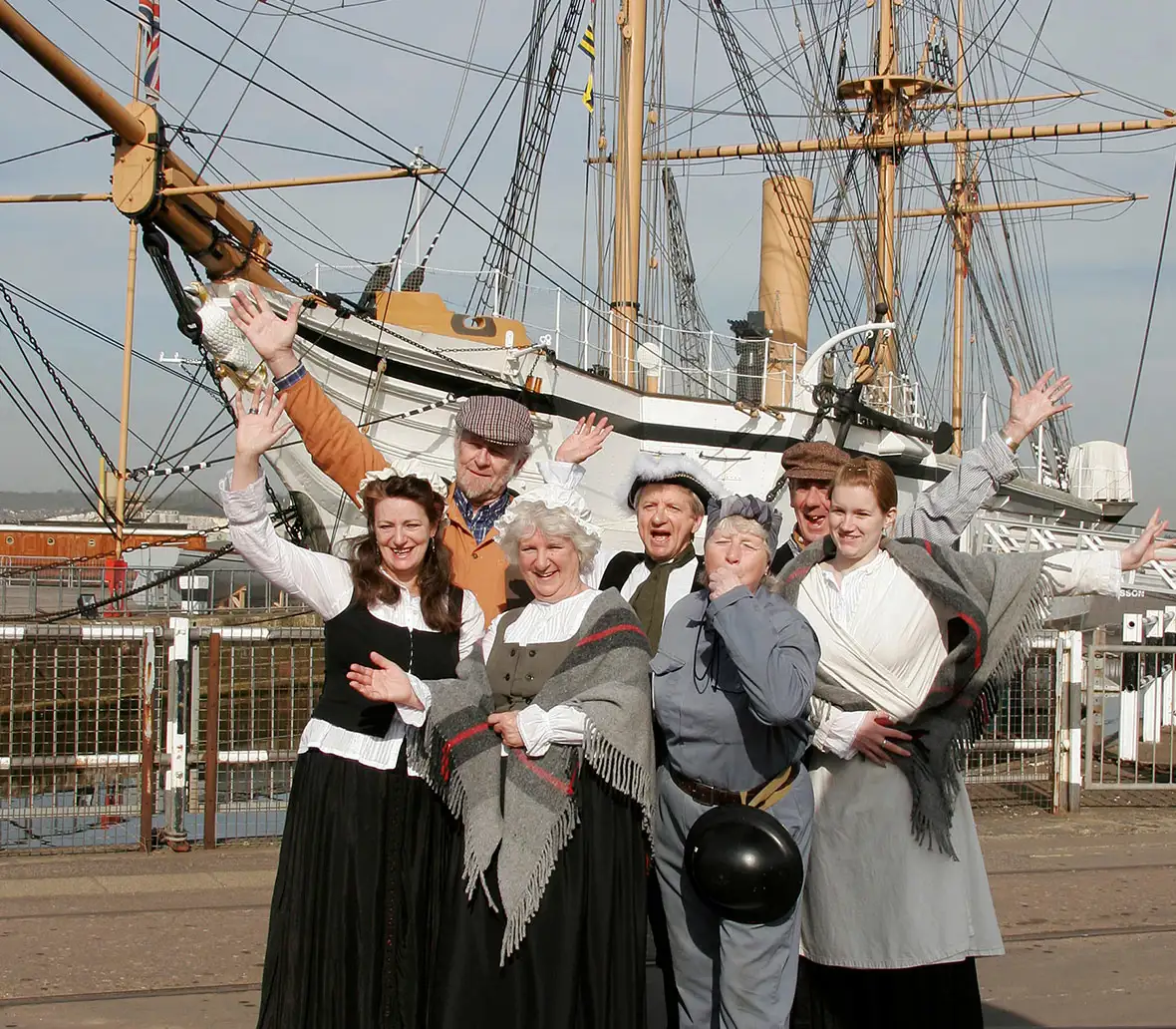 Groep mensen in negentiende-eeuwse kleding poseert voor een historisch zeilschip