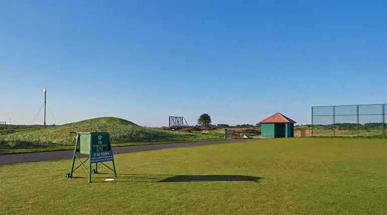 Vlakke golfbaan, op de achtergrond een kleine heuvel, een gebouwtje en een hek